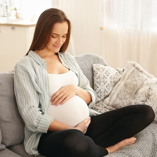 Love, family, motherhood and pregnancy concept. Portrait of charming young dark haired married woman expecting baby, touching her belly, being seventh month pregnant, having happy expression